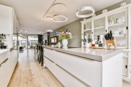Contemporary minimalist style interior design of light studio apartment with wooden table and chairs in dining zone between open kitchen and living room with white walls and parquet floor